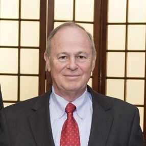 Dennis-Denny-Wist-Head-Shot man in black suit, with red tie