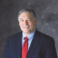 IMPACT Board Member Larry Miller, Headshot of man in suit smiling at camera