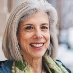 Susan Silk Headshot. Woman smiling at camera, light hair, green blouse
